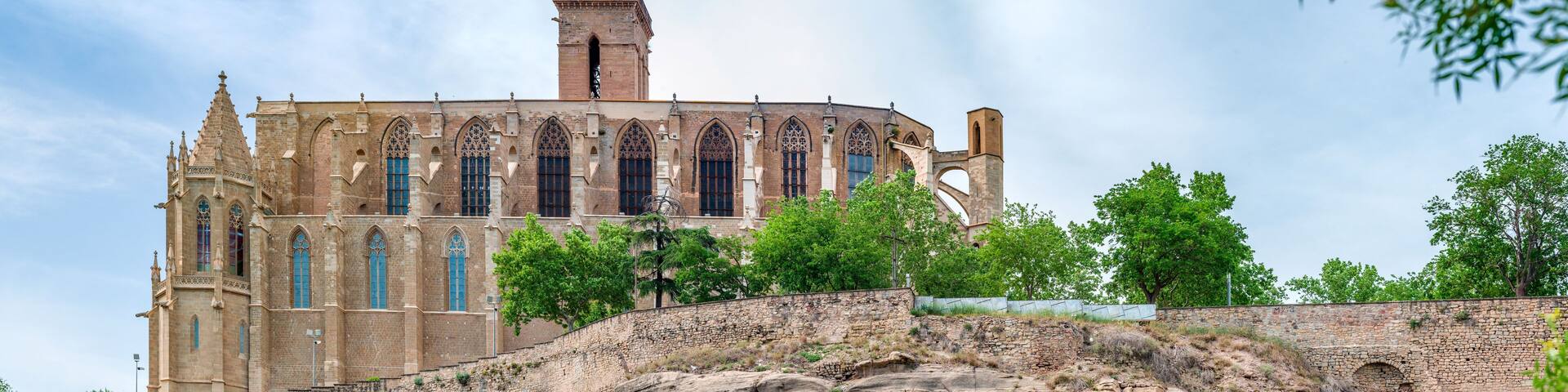 A historic building with Gothic architecture, perched atop a rocky cliff with lush greenery.