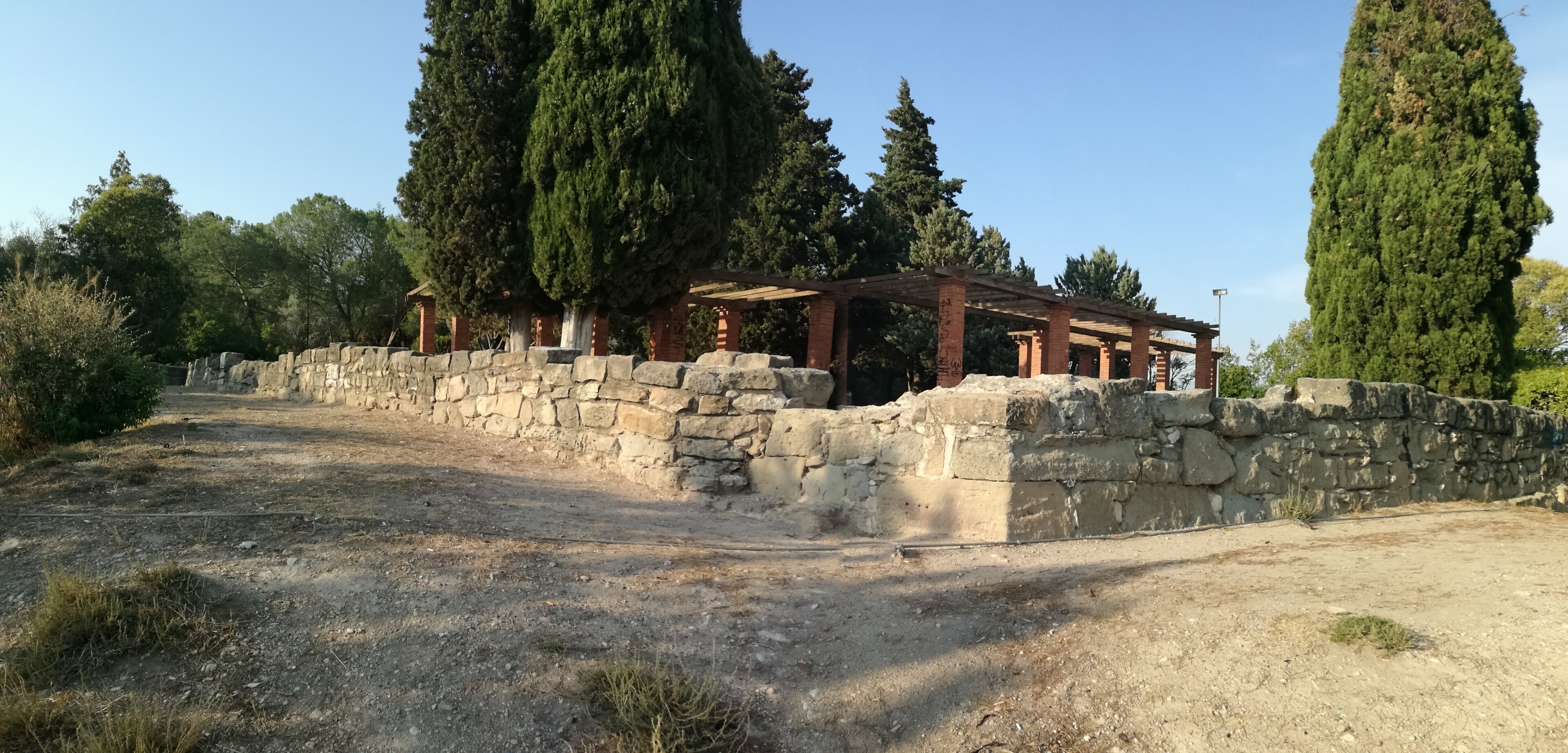An ancient stone wall with a wooden pergola structure.