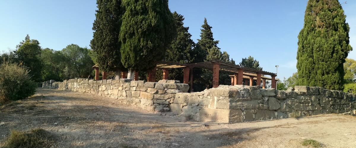 An ancient stone wall with a wooden pergola structure.