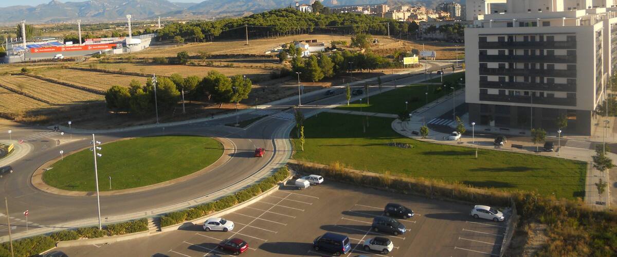 A parking lot with cars, a roundabout, and a building with a modern design.
