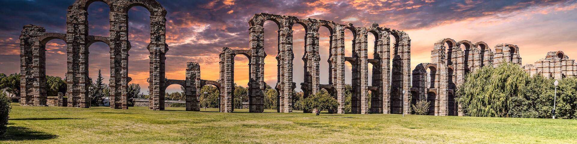 Ancient stone ruins with arches, set against a dramatic sunset sky.