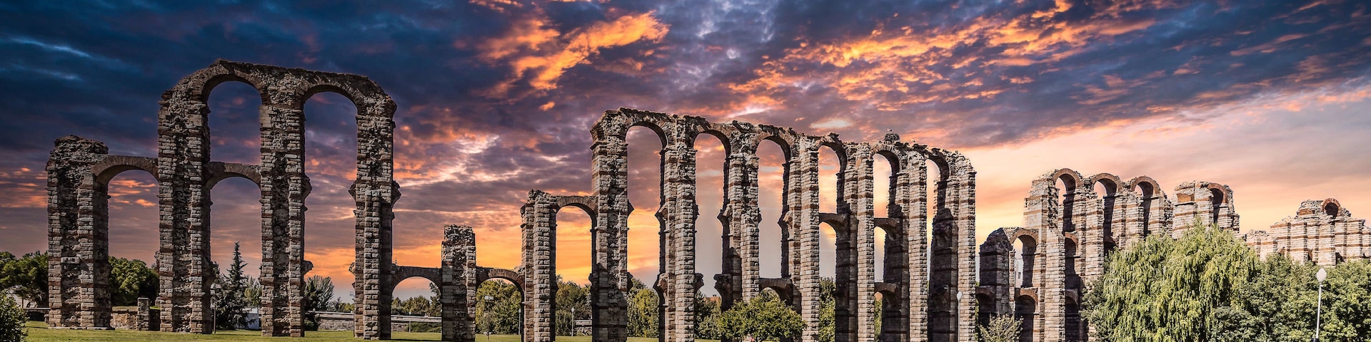Ruinas antiguas de piedra con arcos, al atardecer con un cielo espectacular.