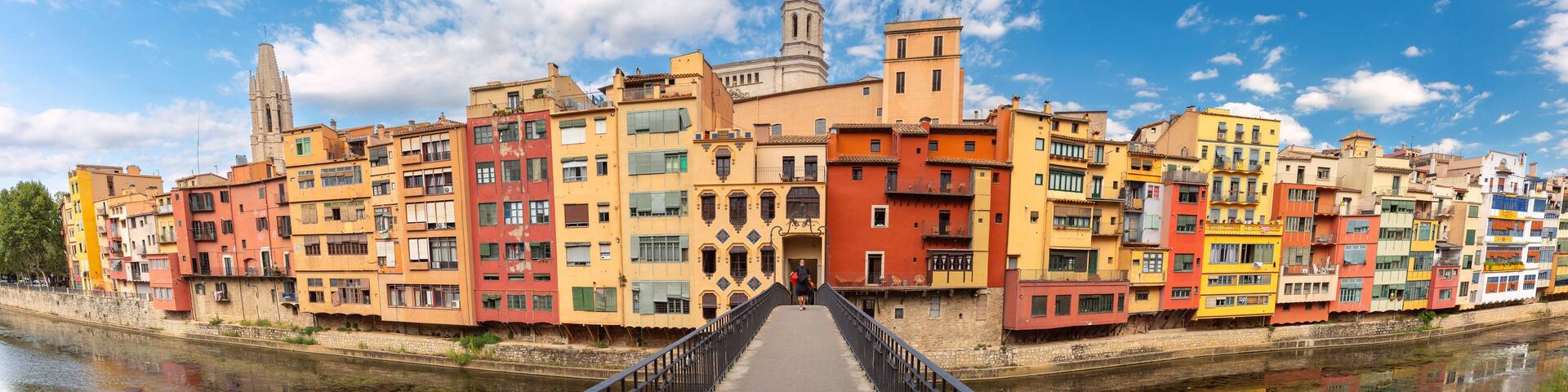 A colorful waterfront promenade with a bridge leading to a historic building with a bell tower.