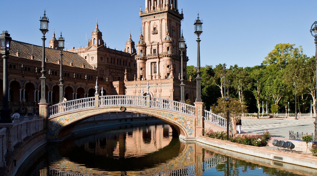 A historic building with a prominent tower, a decorative bridge, and a calm water body reflecting the architecture.