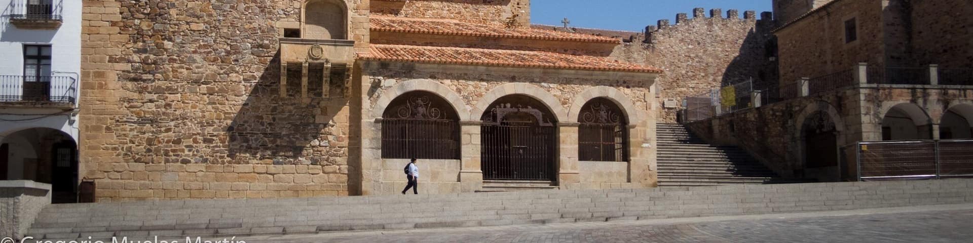 A historic stone building with a tower, arched windows, and a staircase leading to a gate.
