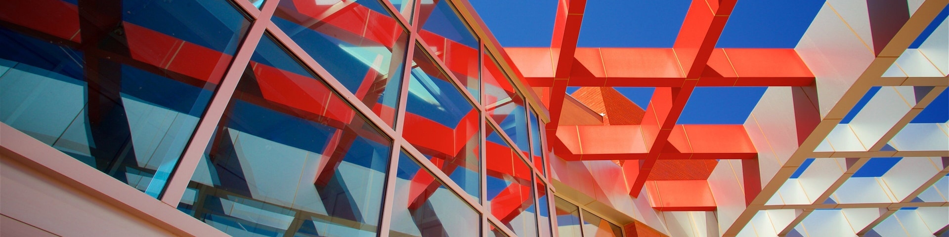 Un edificio moderno con fachada de vidrio y elementos estructurales geométricos en rojo y blanco.