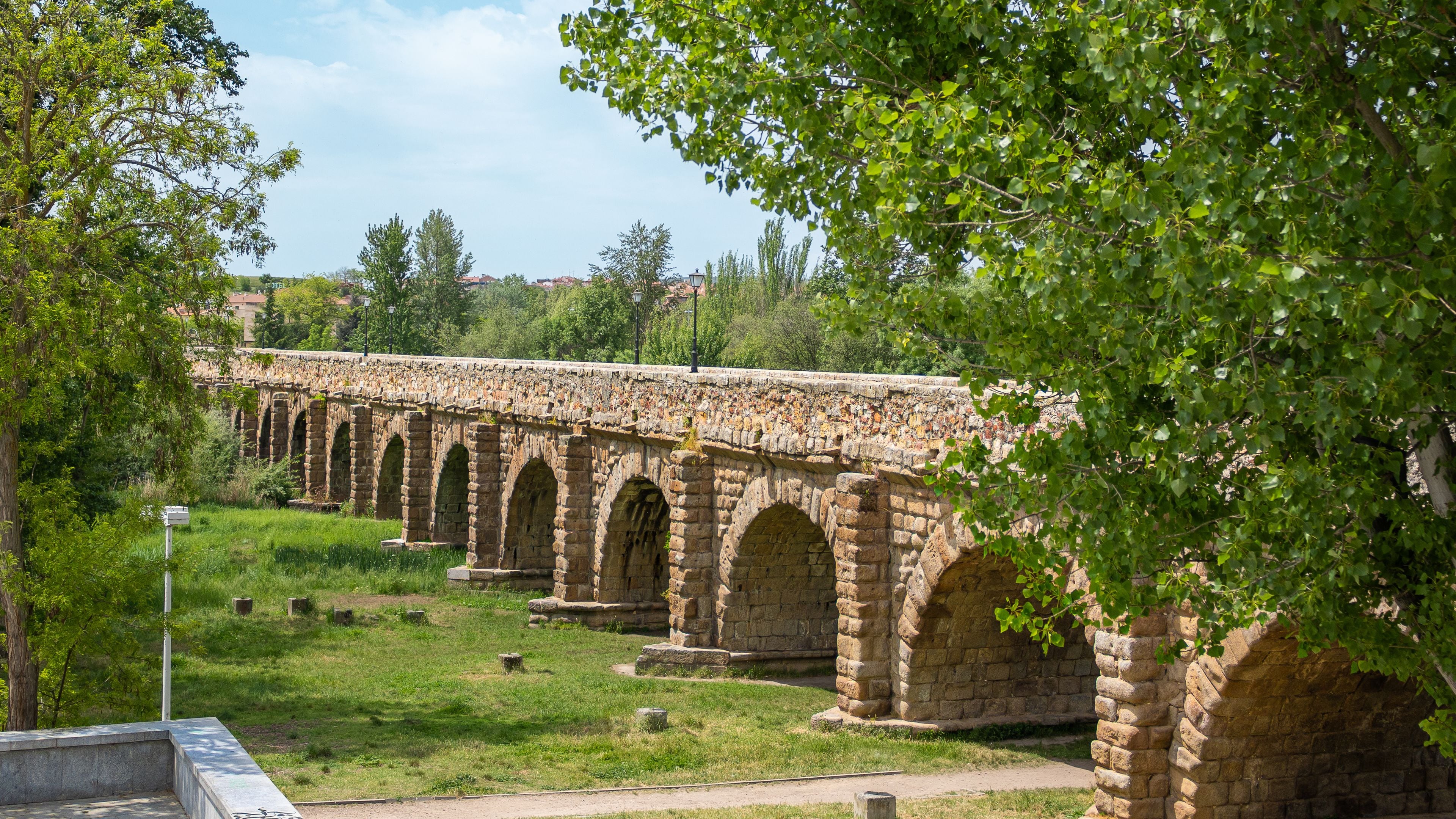 A stone bridge with multiple arches, surrounded by greenery and trees.