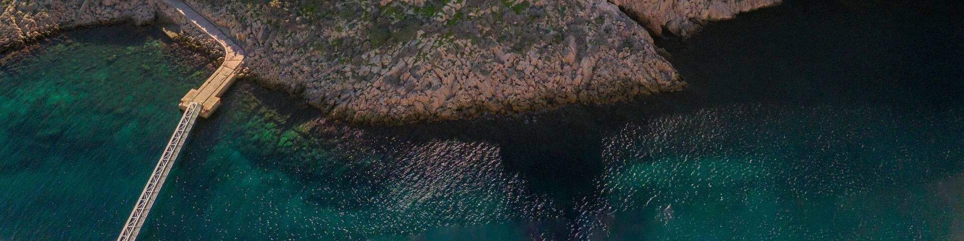 An aerial view of a coastal island with a lighthouse, a road, and a pier.