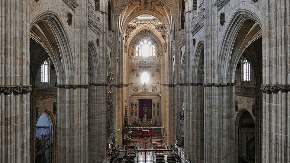 Interior imponente de una catedral con altos techos abovedados, intrincadas esculturas de piedra y un altar central.