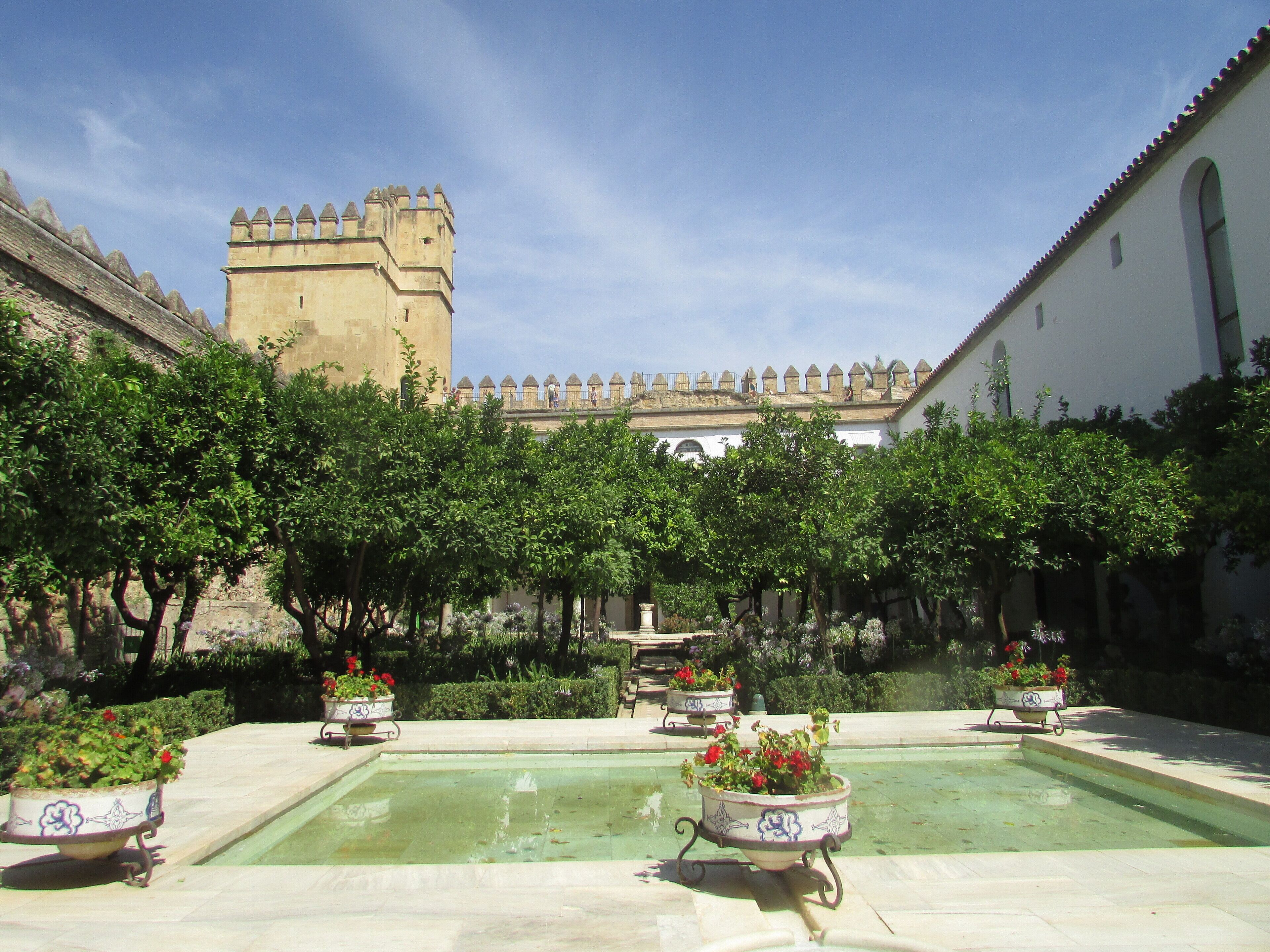 A courtyard with a fountain, potted plants, and a castle in the background.