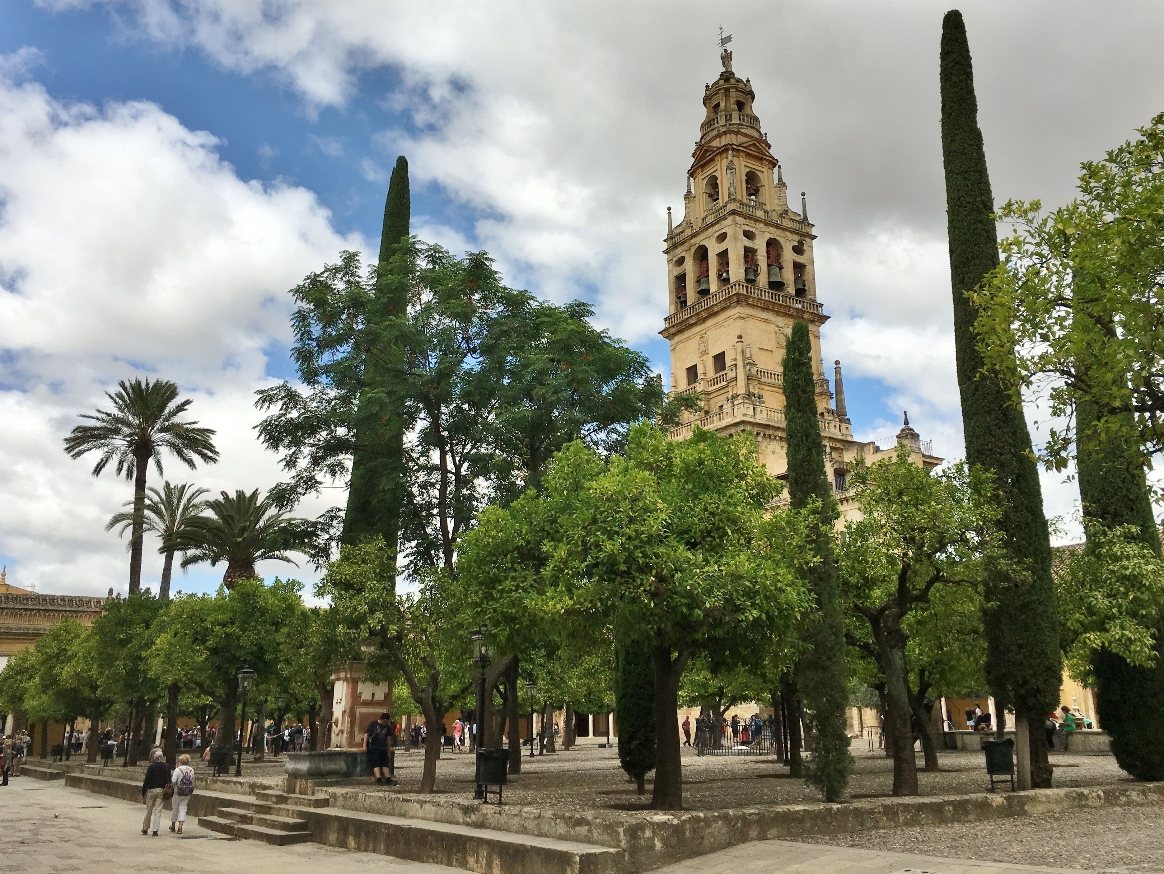 Una torre histórica con una campana, rodeada de árboles y una plaza con gente.