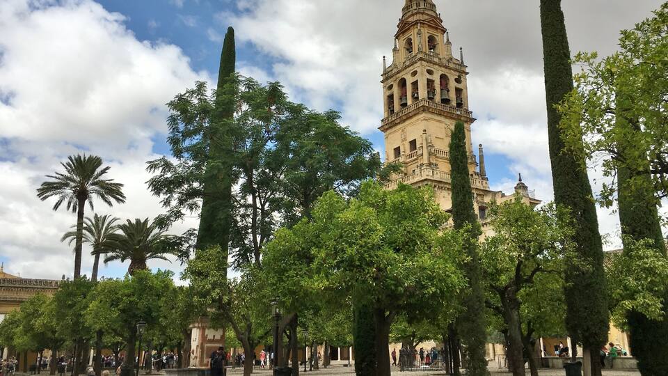 Una torre histórica con una campana, rodeada de árboles y una plaza con gente.