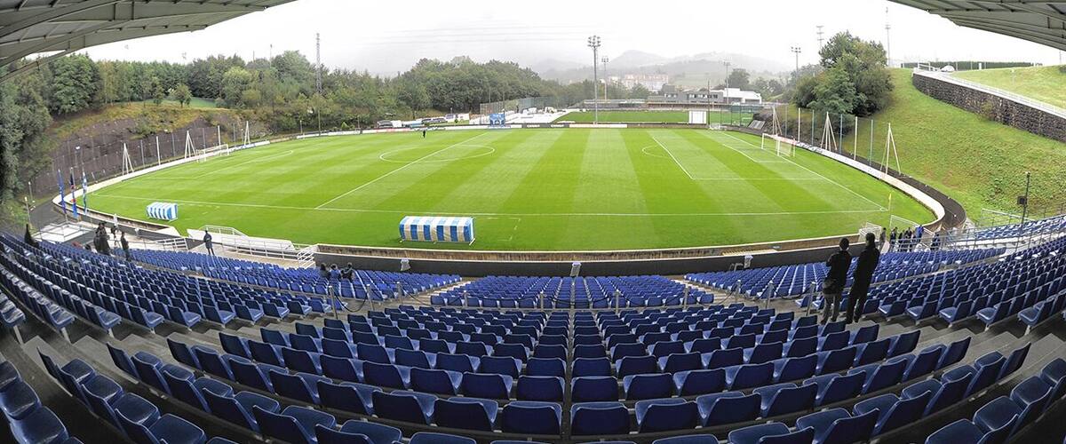 A large, empty stadium with blue seats and a green field.