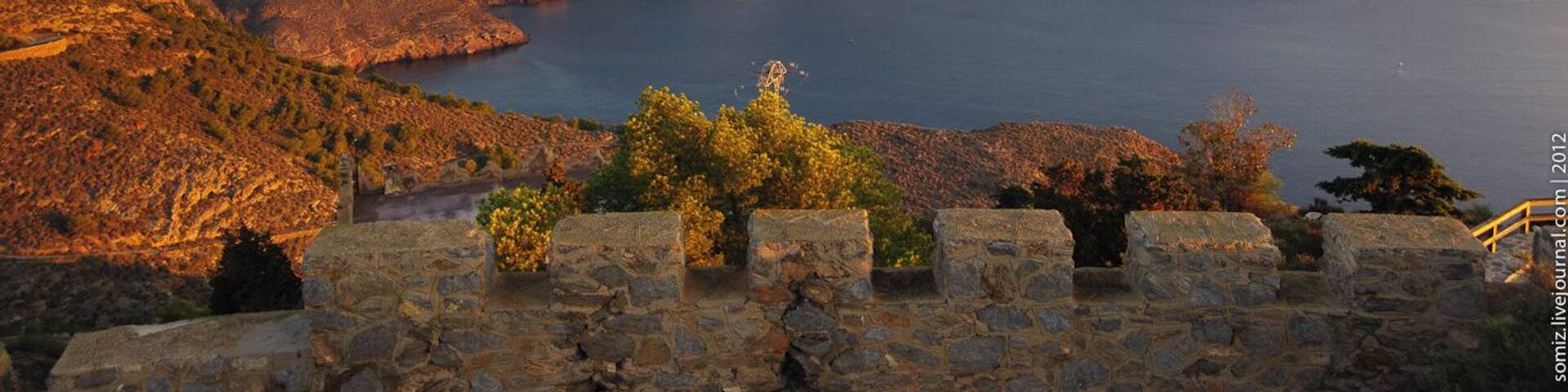 A mountainous landscape with a body of water, stone walls, and trees.