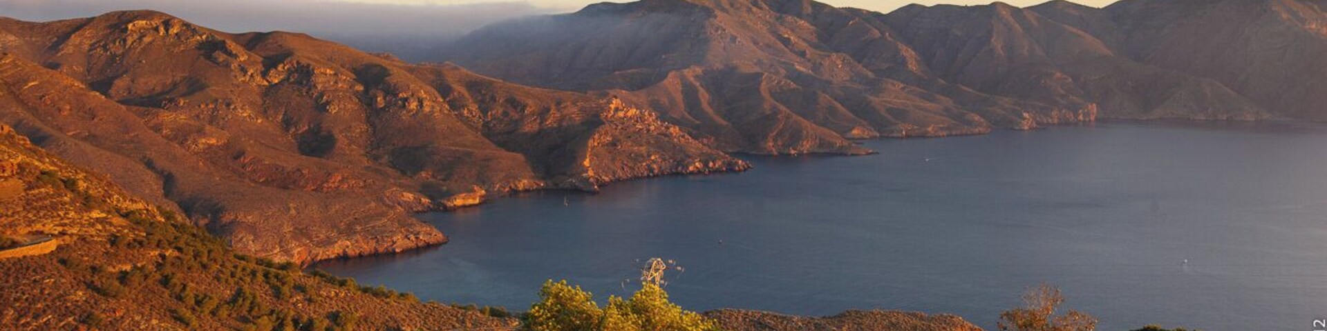 Paisagem montanhosa com um corpo de água, muros de pedra e árvores.