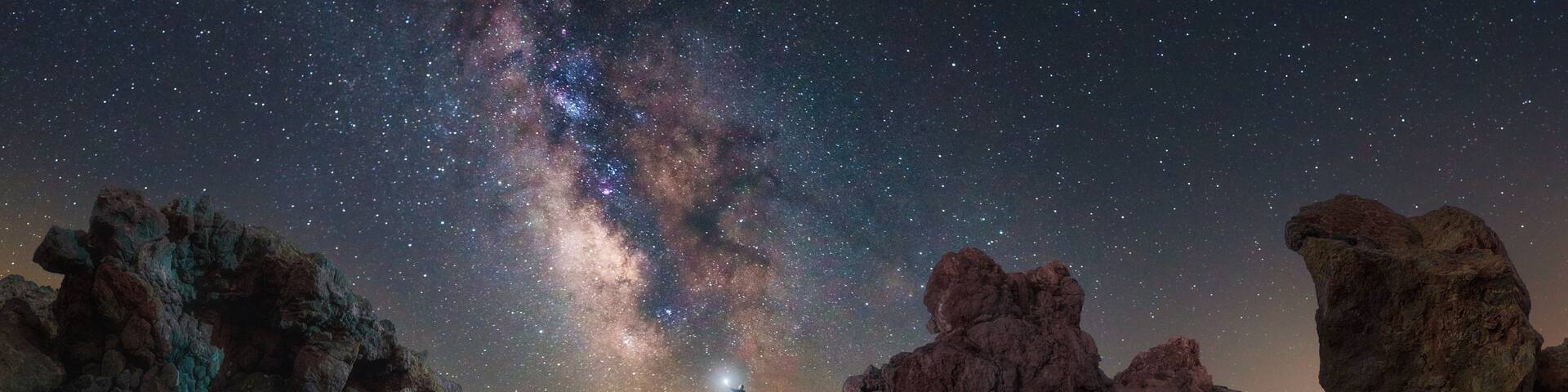 A night scene with a starry sky, rocky formations, and a person with a flashlight.