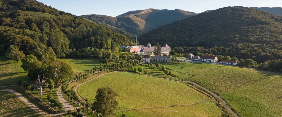 Paisatge rural amb turons ondulats, un camí sinuós i una finca gran amb diversos edificis.