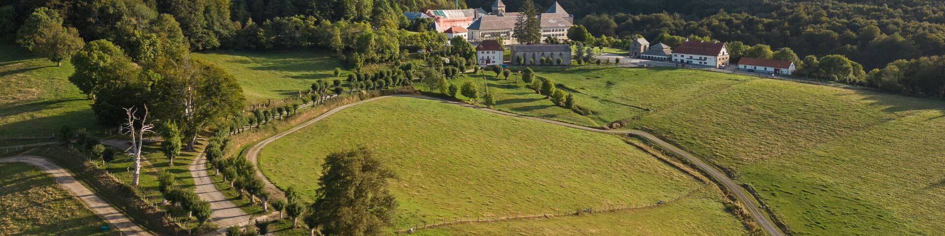 A rural landscape with rolling hills, a winding road, and a large estate with multiple buildings.