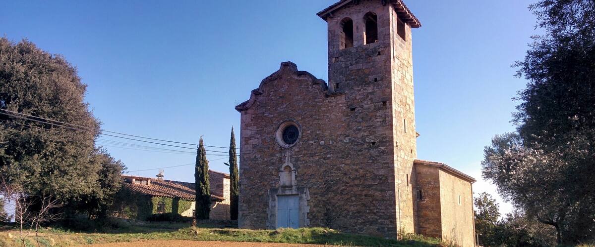 A stone church with a bell tower, surrounded by trees and a field.
