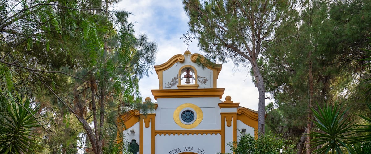 A church with a bell tower, surrounded by lush greenery.