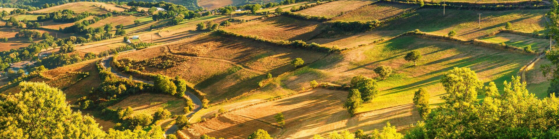 A mountainous landscape with rolling hills, fields, and a valley shrouded in mist.