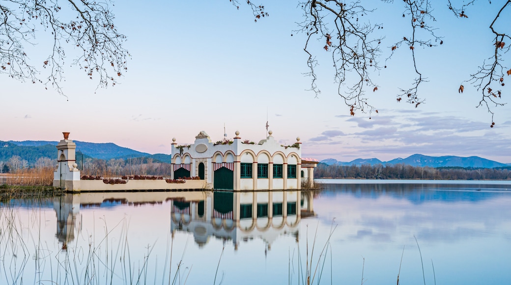 Un lago tranquilo con una casa flotante en el centro, rodeado de aguas apacibles y montañas al fondo.