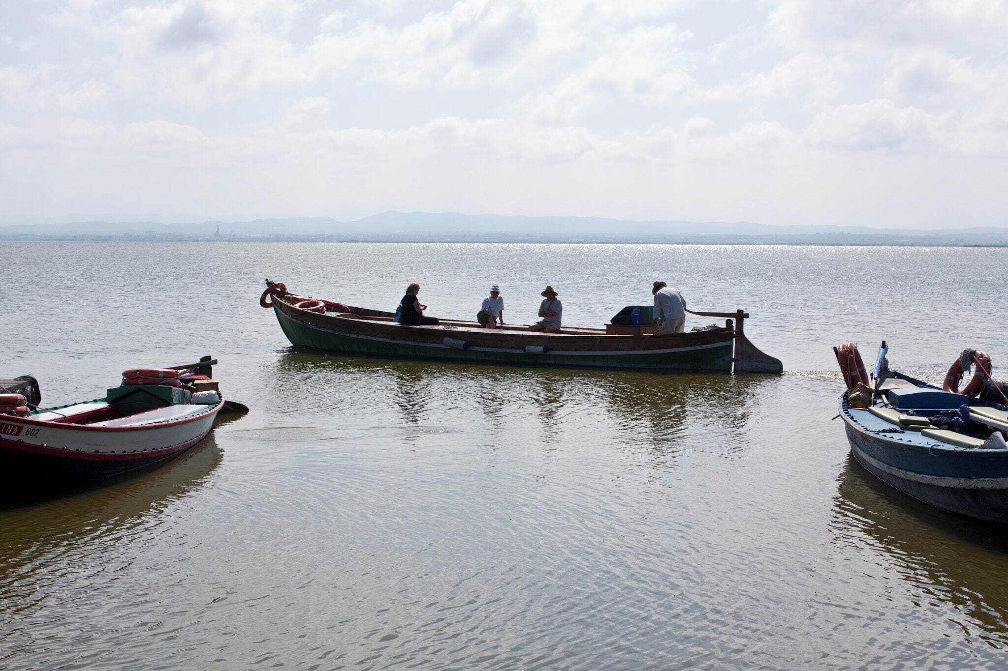 A calm lake with several boats, including a large traditional boat with people on it.