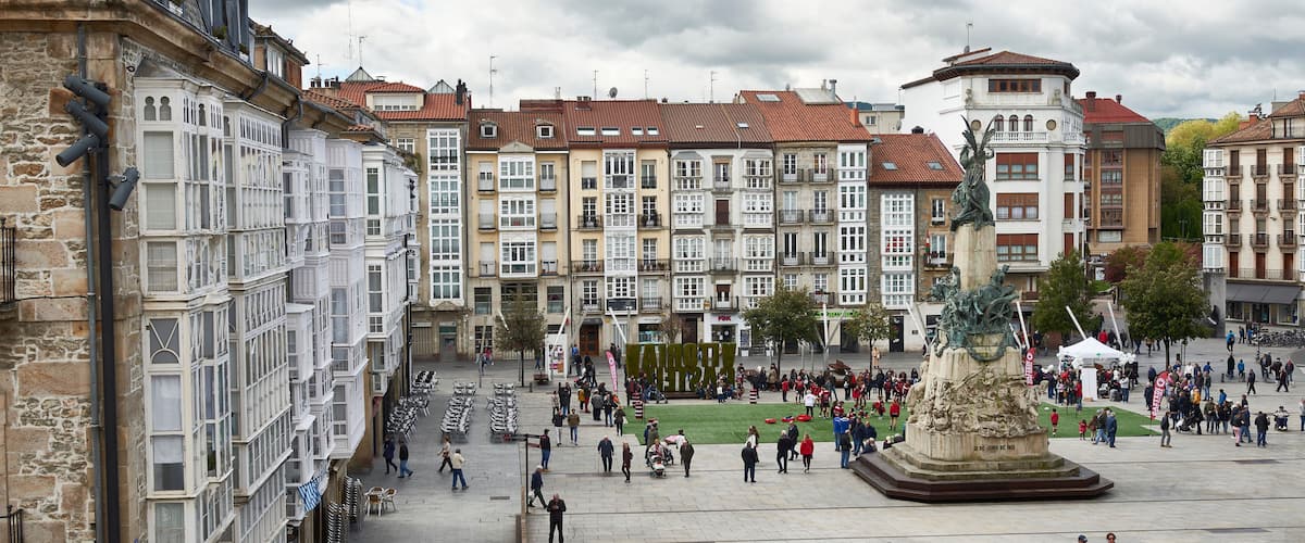 Una plaza animada con edificios históricos, una fuente central y una multitud de gente.