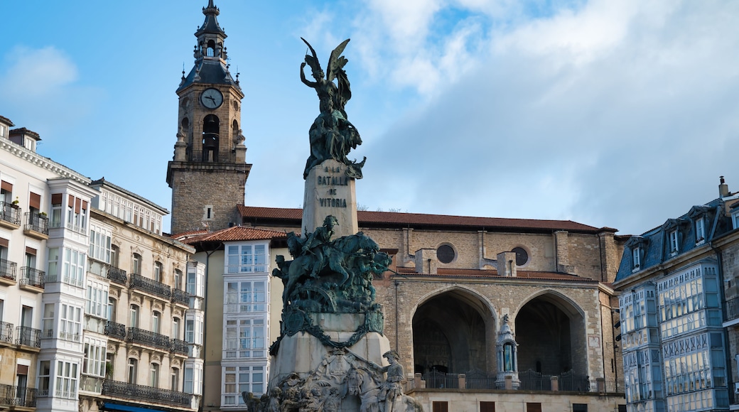 A historic square with a clock tower, a statue, and classical architecture.