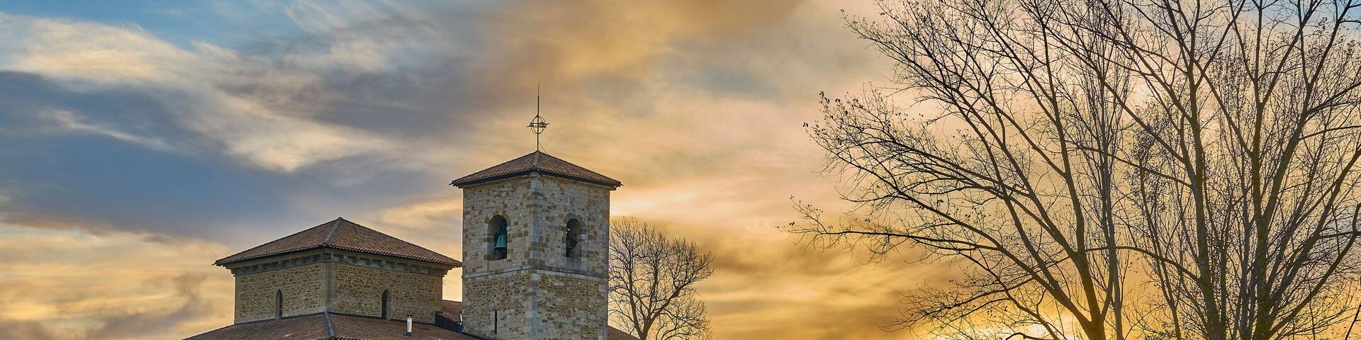 A stone church with a bell tower and a large open field in the foreground.