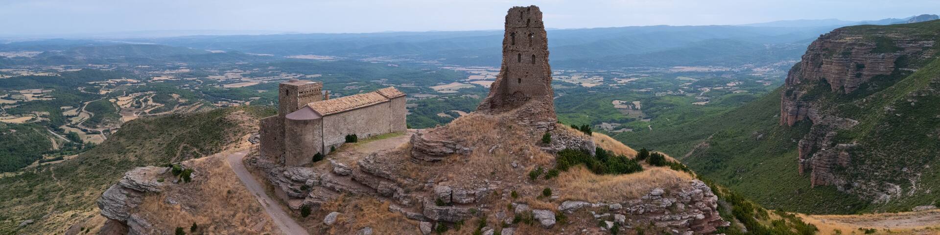 An ancient stone fortress on a hilltop overlooking a valley.
