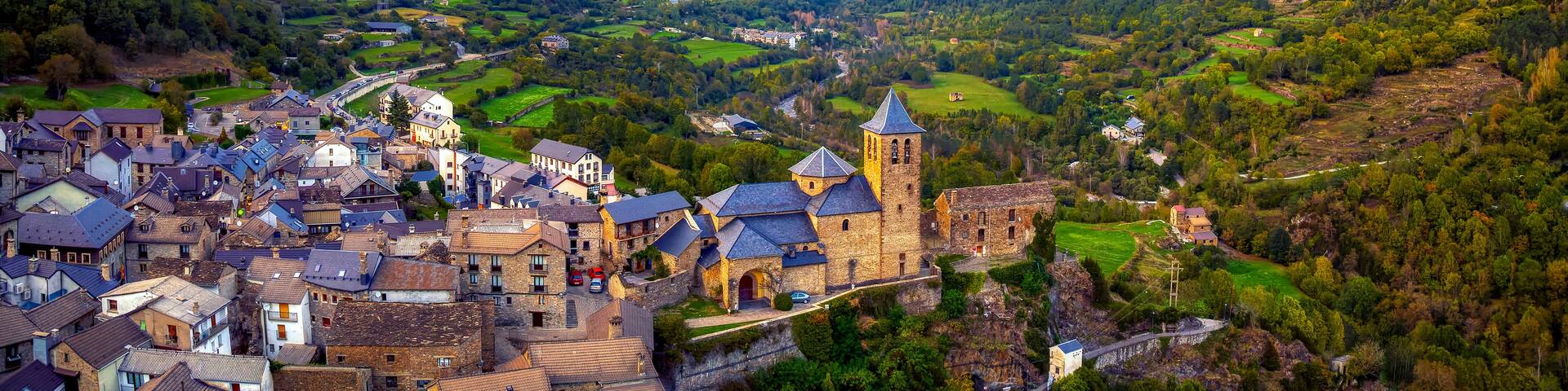 A mountainous landscape with a village nestled in a valley, featuring a prominent church tower and lush greenery.
