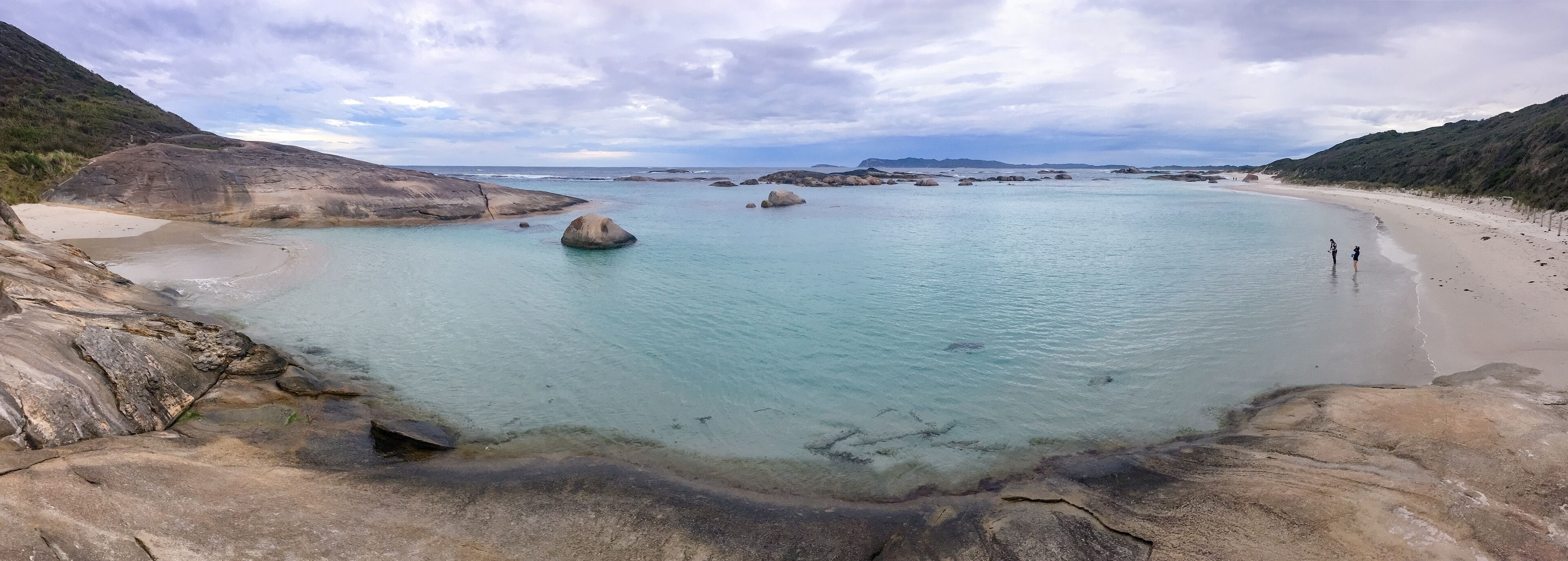 A coastal landscape with clear turquoise waters, rocky formations, and a sandy beach.