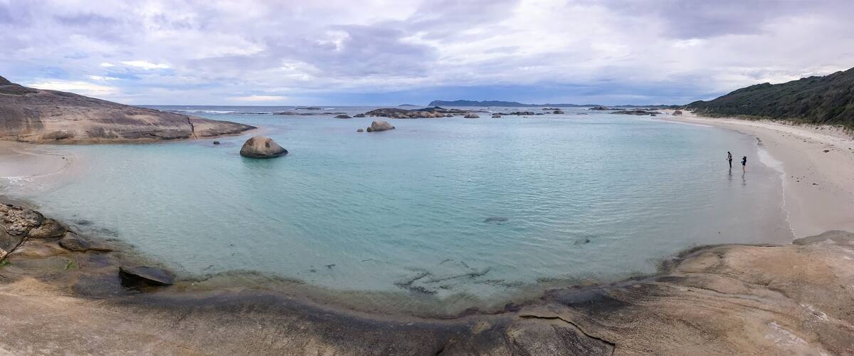 A coastal landscape with clear turquoise waters, rocky formations, and a sandy beach.
