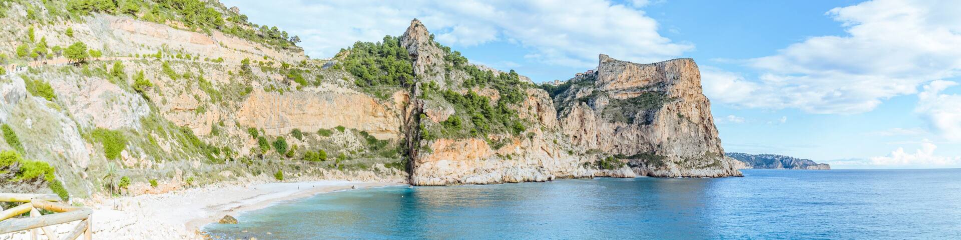 Benitachell, Spain: Rocky coastline with beach and blue sea under sky