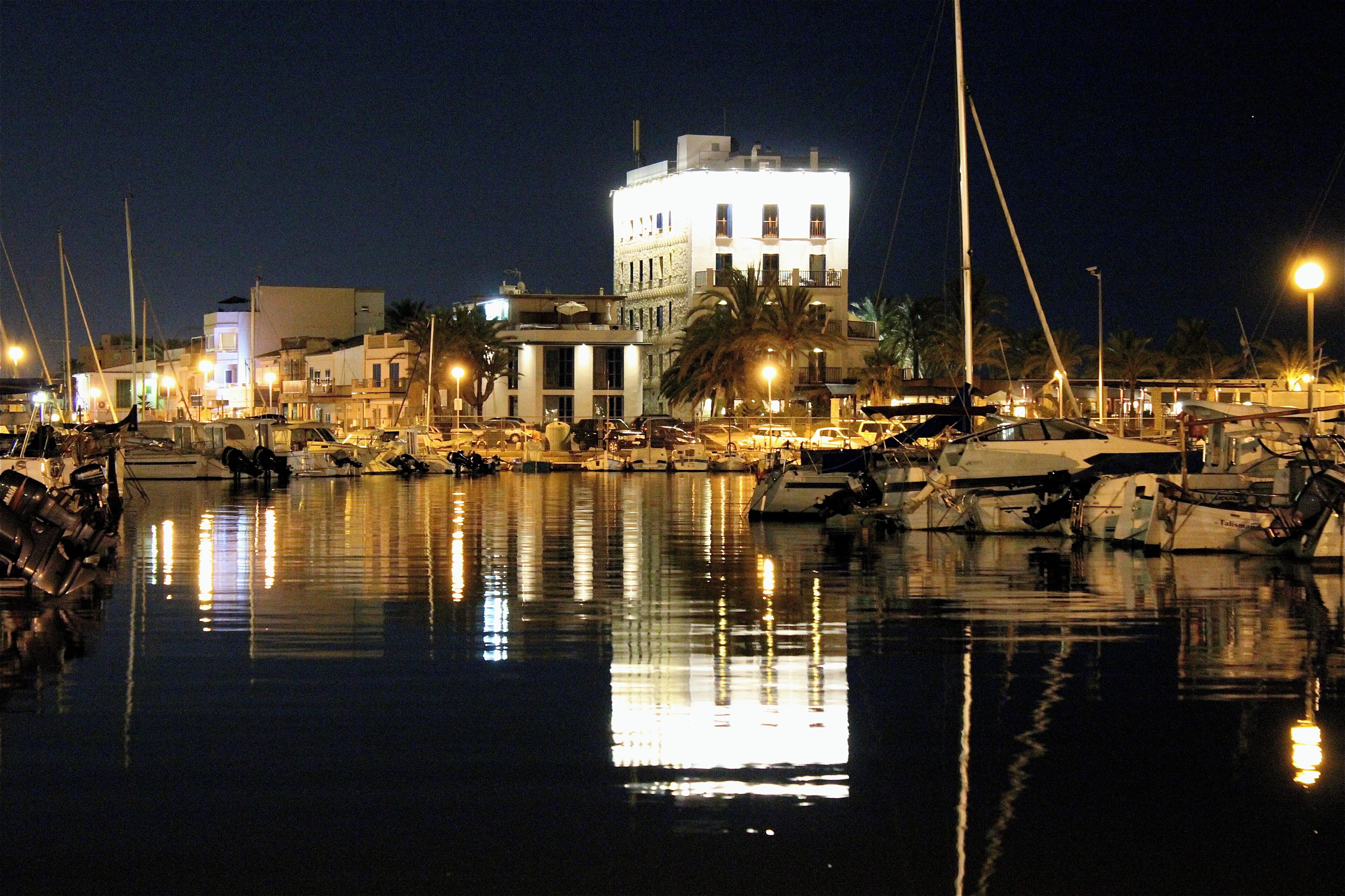 Uma marina à noite com barcos atracados e reflexos na água.