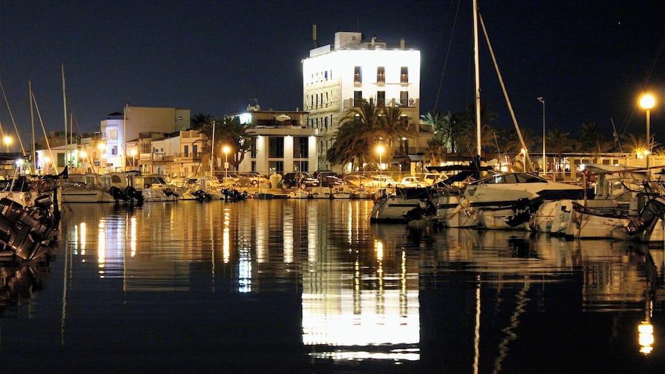 Uma marina à noite com barcos atracados e reflexos na água.