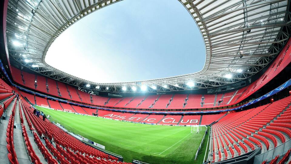 A large stadium with red seating and a green field.