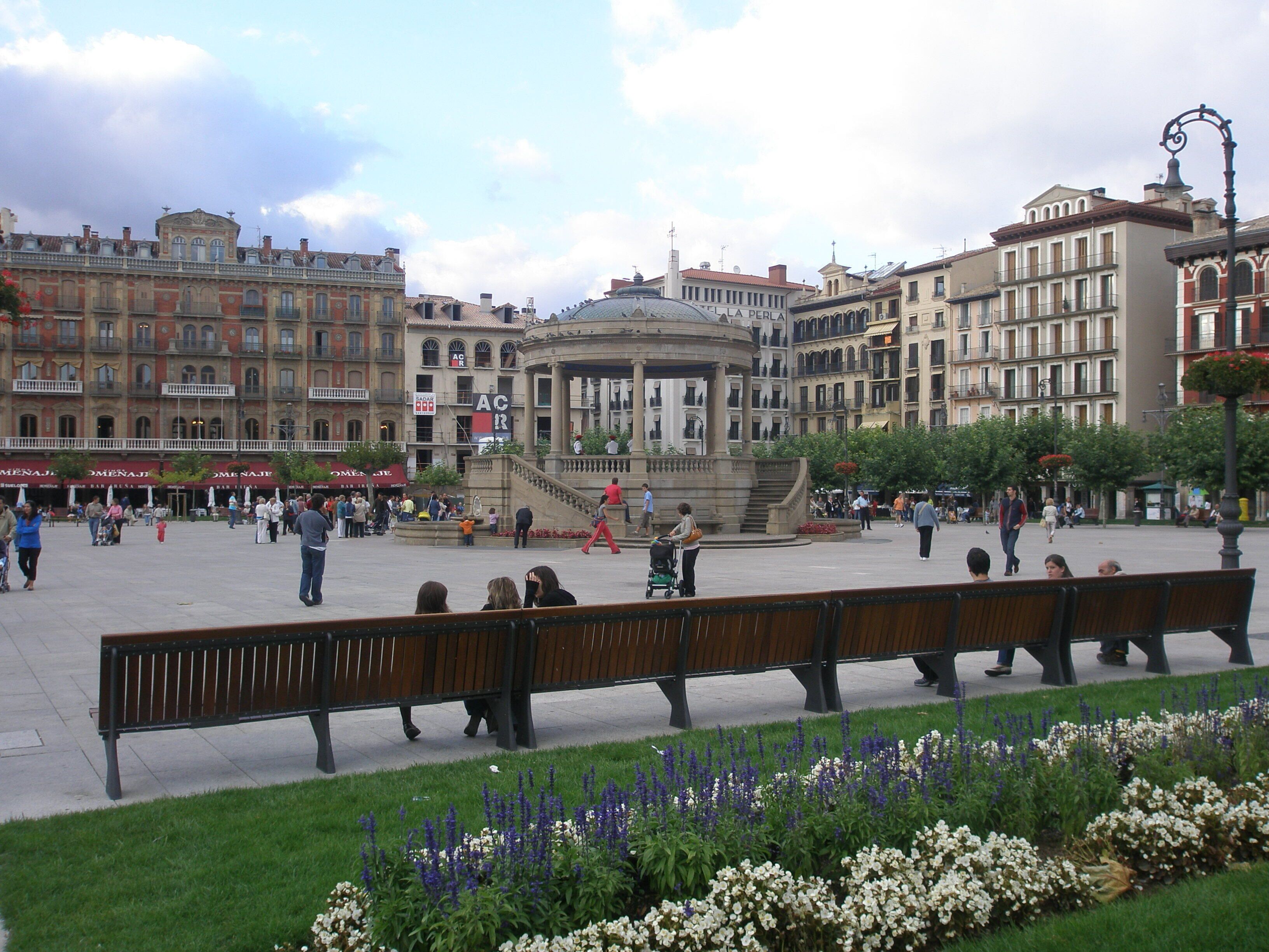 Una plaza pública con una fuente central, rodeada de edificios históricos y bancos.