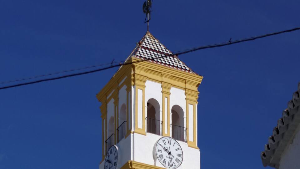 Une tour d’horloge jaune, surmontée d’une girouette, se dressant sur un ciel bleu dégagé.