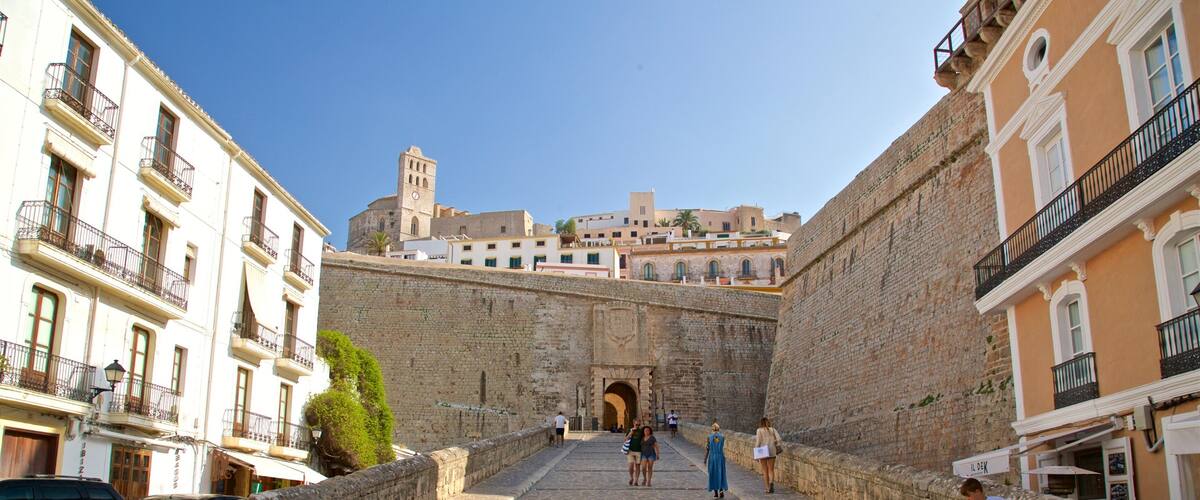Una escalera de piedra que conduce a una antigua puerta, flanqueada por edificios antiguos y un cielo azul despejado.