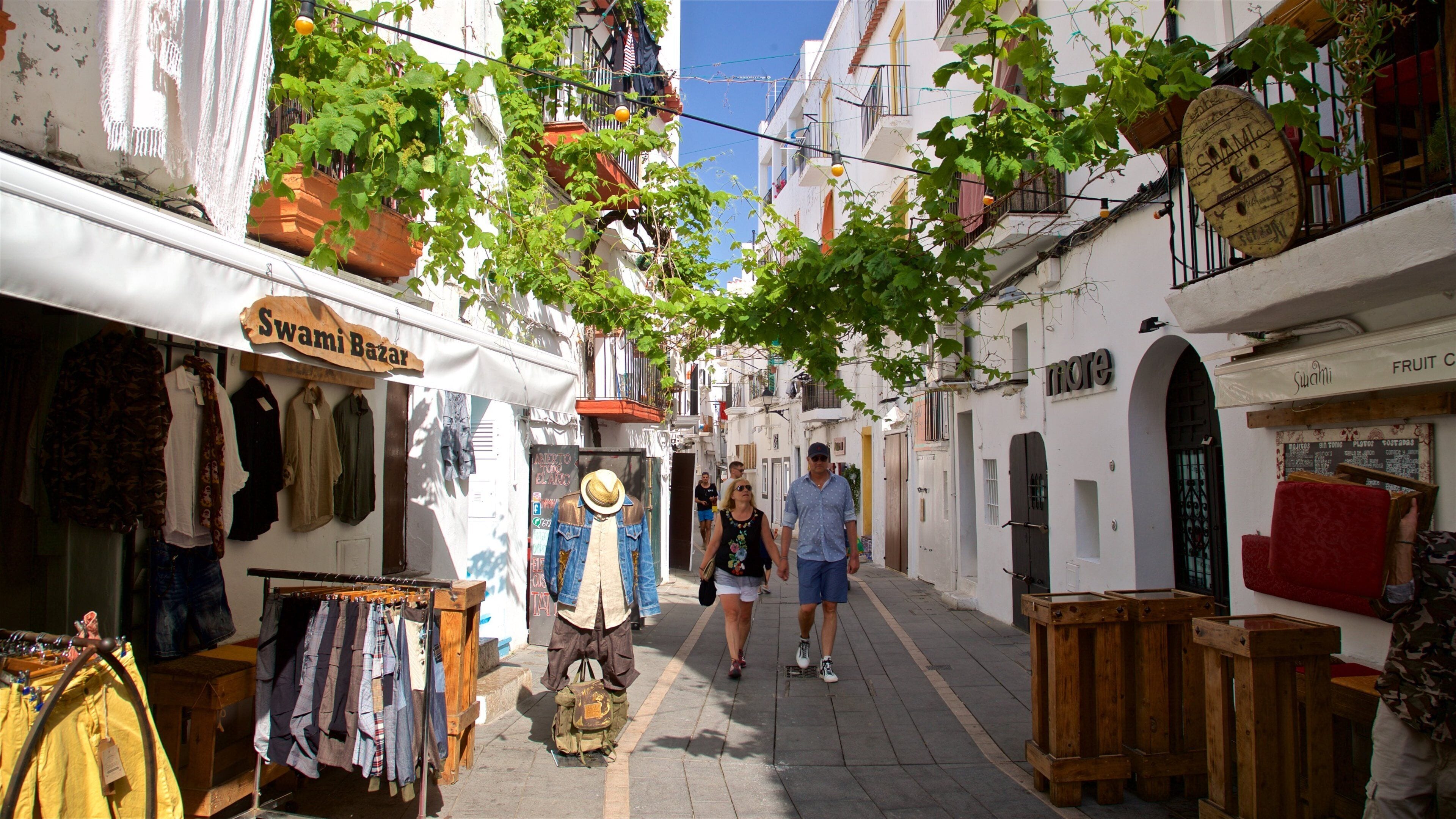 A narrow street with shops, including a fruit stand and a clothing store.