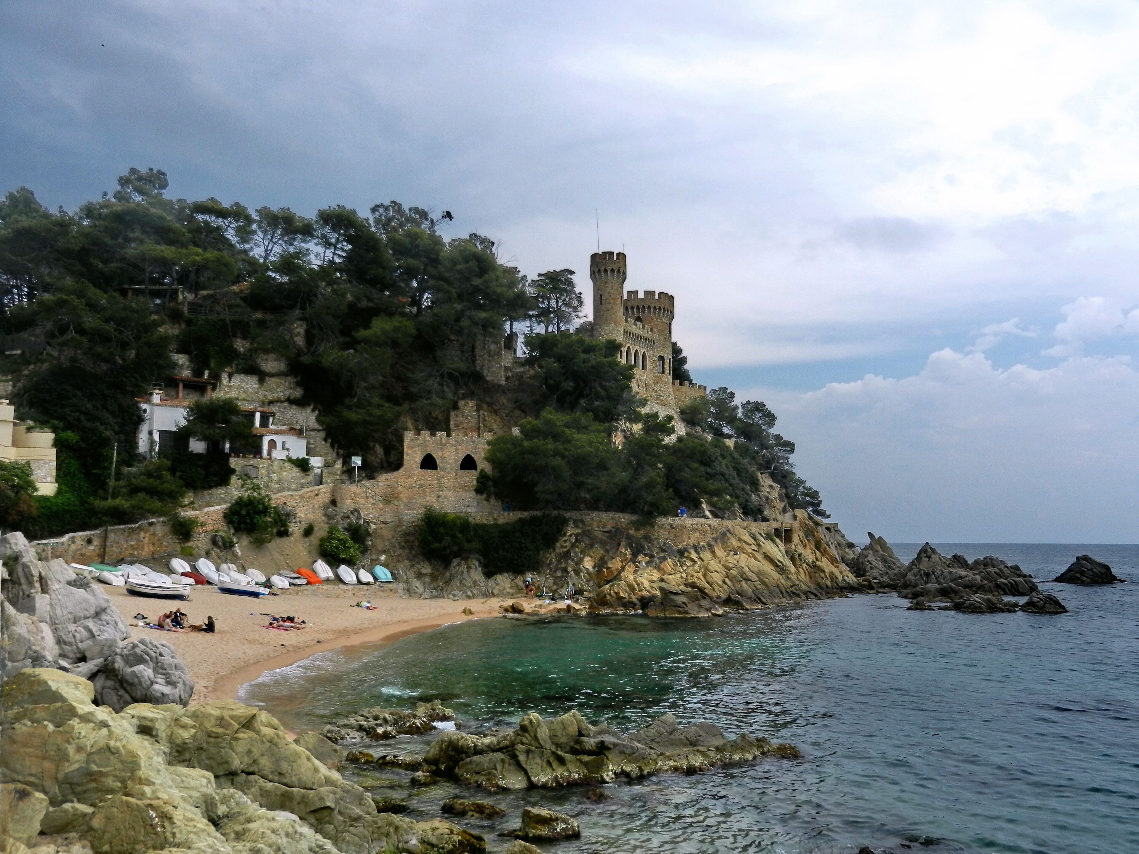 A coastal area with a castle on a cliff, beach, and boats.