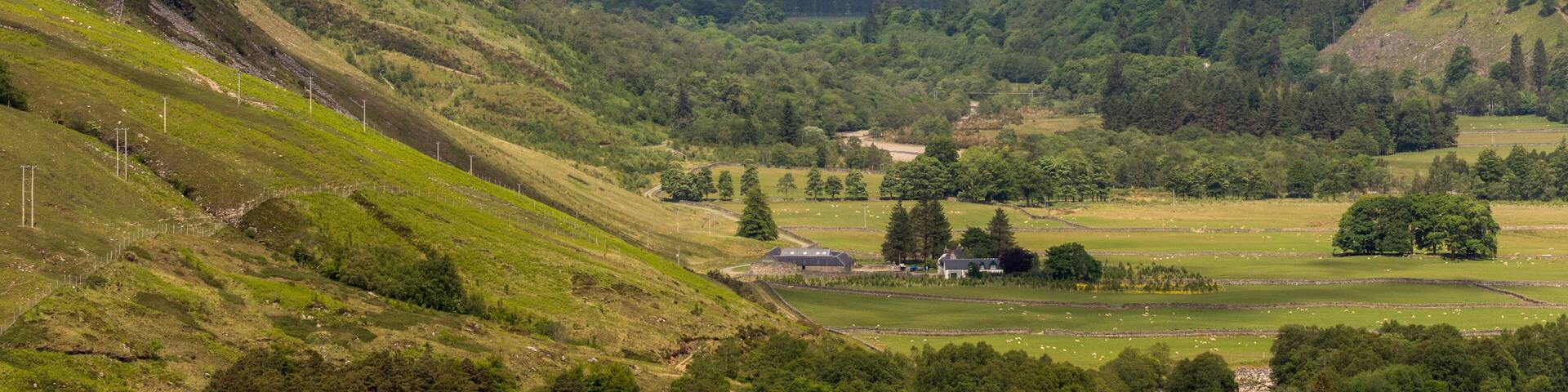 Braemore, Scotland - June 8, 2012: West of Corrieshalloch Gorge along A832 from height look upon Loch Broom under cloudy cloudscape. Green forested mountains. Meadows on slopes and valley.