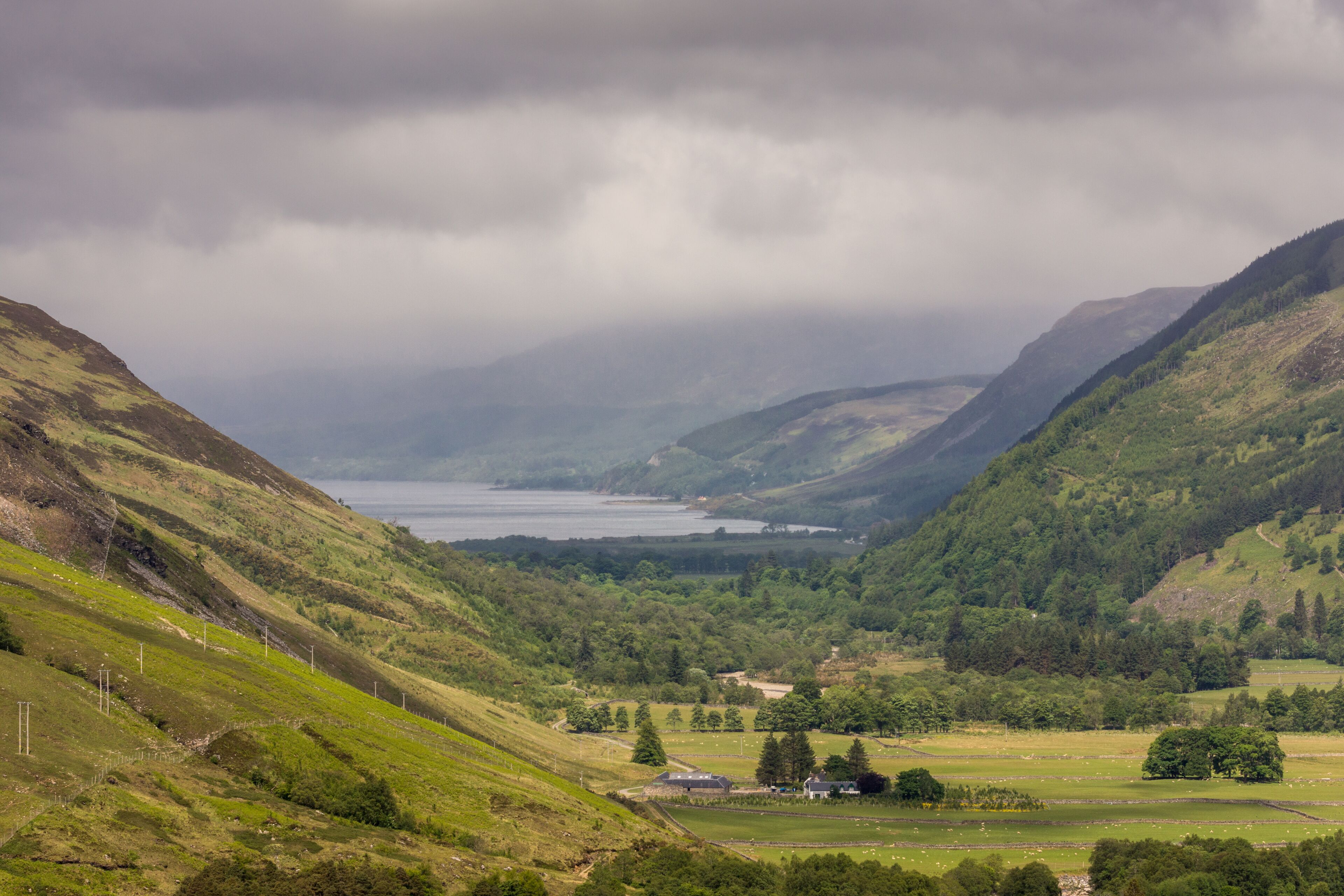 A valley with a lake, green hills, and a small house.