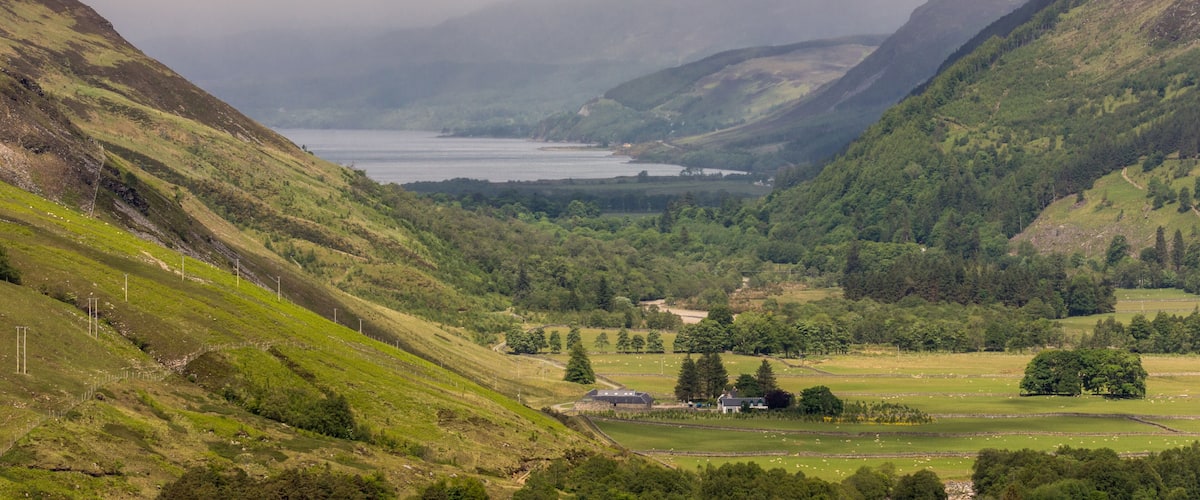 A valley with a lake, green hills, and a small house.