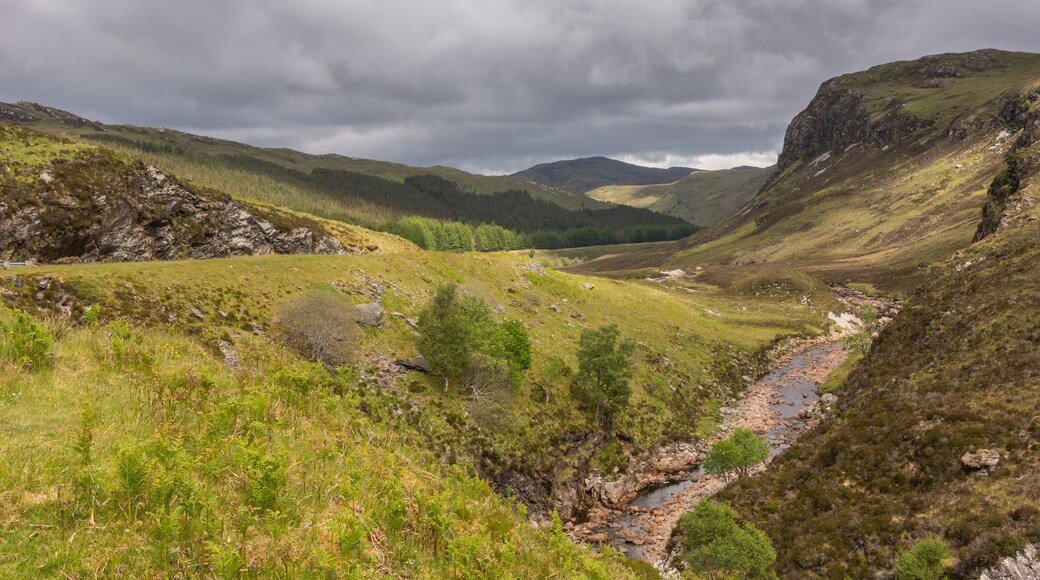 Braemore, Scotland - June 8, 2012: Dundonnell Rvier along A832 road offers bronwn rocks and grassy hills under dark cloudscape. Hills in back.