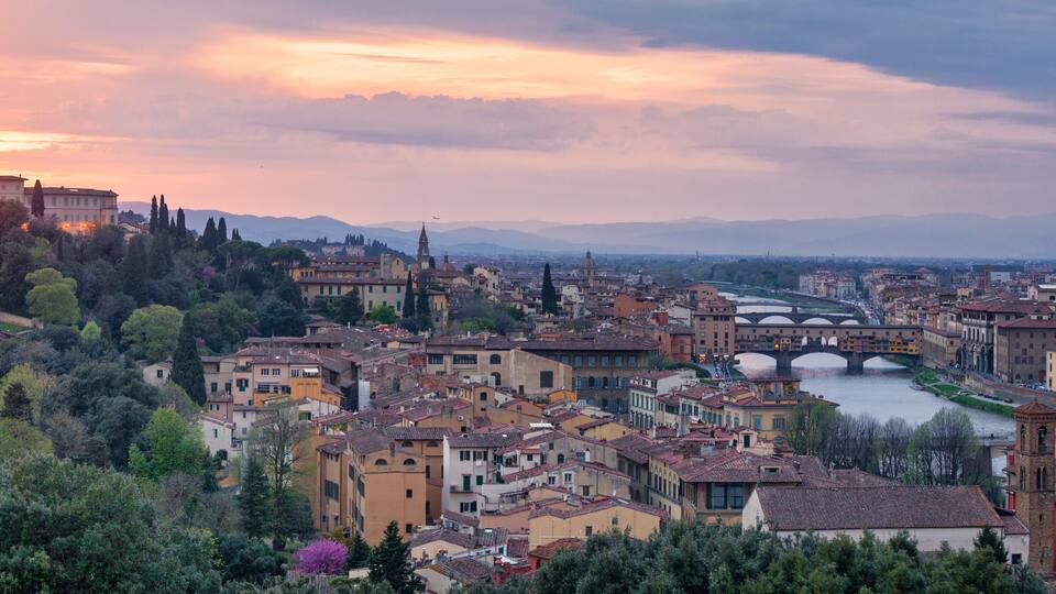 A cityscape with a river, a bridge, and mountains in the background.