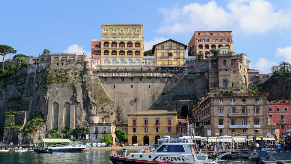 A coastal town with historic buildings, a marina, and a cliffside.