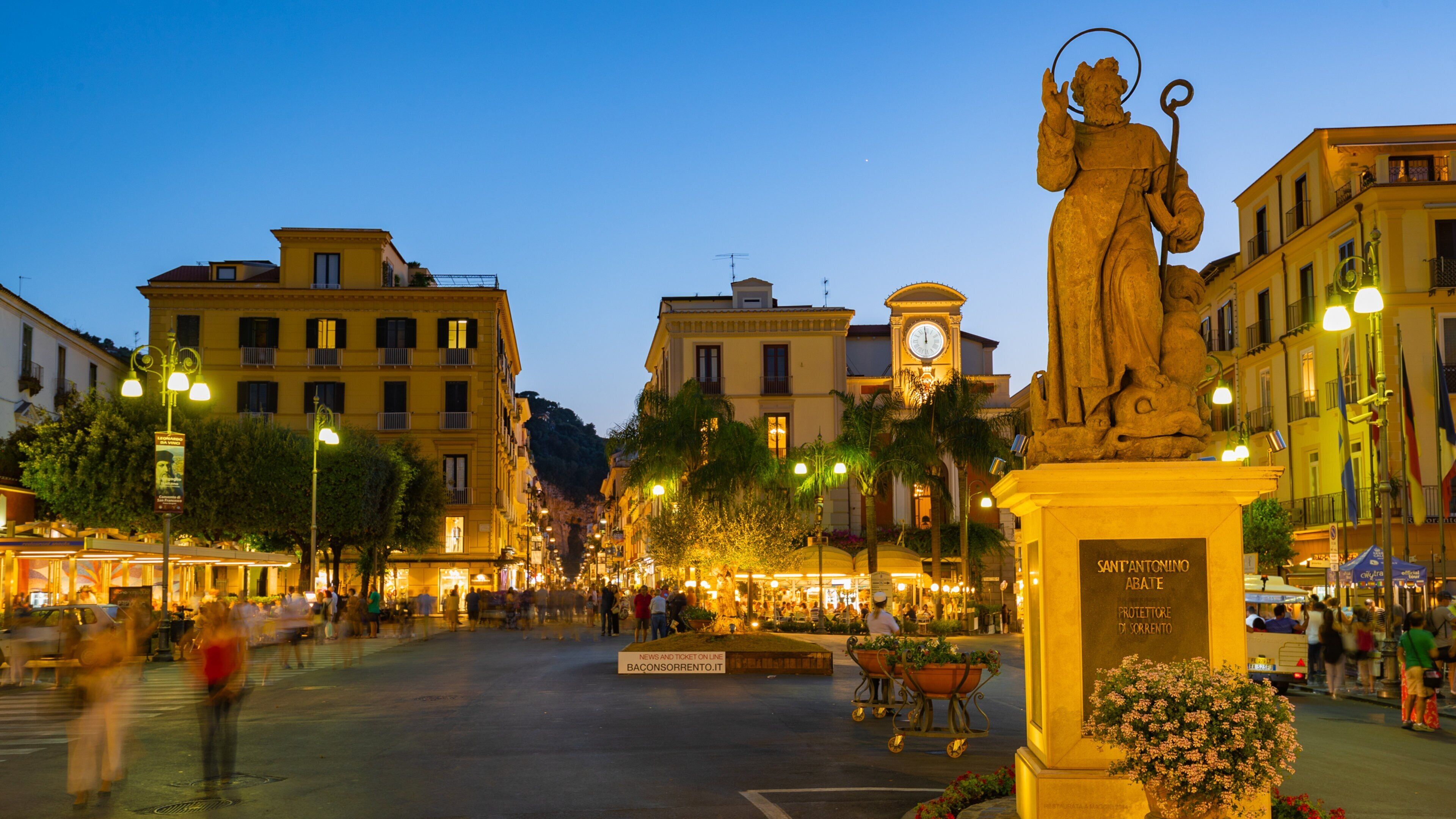 Una piazza vivace con una statua, edifici storici e una torre dell'orologio.